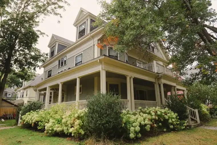 Traditional house with a front porch sitting under the spreading canopy of a large yard tree