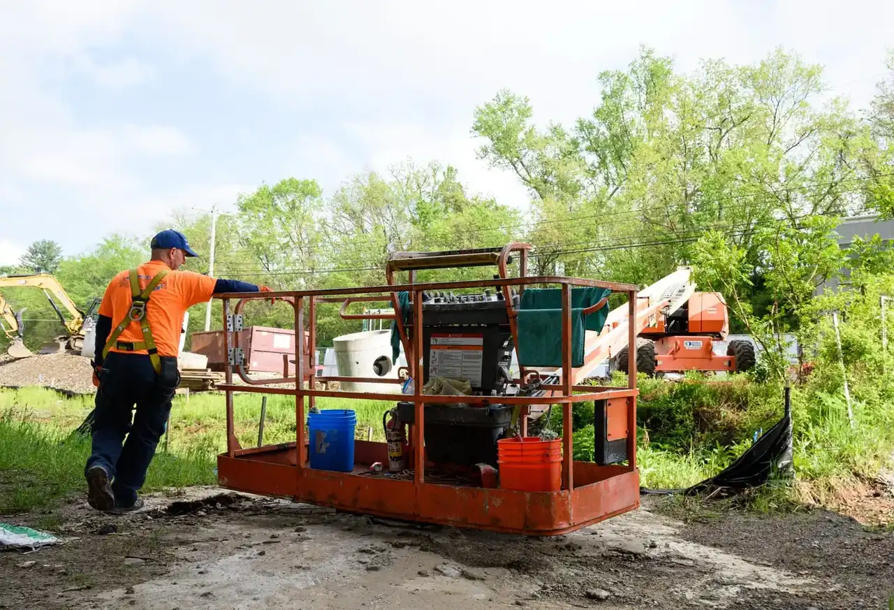Worker in a safety vest beside a lift basket and heavy equipment staged at a job site